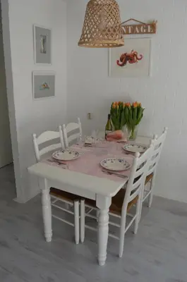 a white dining room table with white chairs and flowers at Sea in Egmond aan Zee