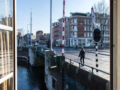 a woman walking down a street next to a river at SWEETS - Willemsbrug in Amsterdam