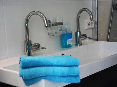 a bathroom sink with two faucets and a blue towel at Holiday Home in Noordwijkerhout near Beach in Noordwijkerhout