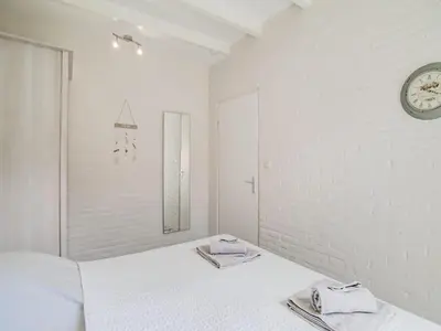a white bedroom with a bed and a clock on the wall at Bungalow in Noordwijk near Beaches in Noordwijkerhout