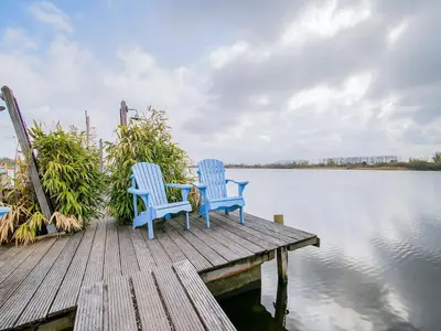 two blue chairs sitting on a dock next to the water at Bungalow in Noordwijk near Beaches in Noordwijkerhout