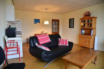 a living room with a black leather couch with red pillows at Bas Apartment Egmond aan Zee in Egmond aan Zee