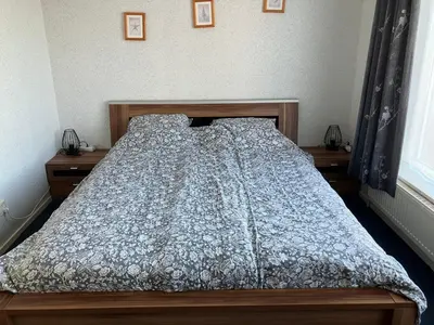 a bed in a bedroom with two night stands and two windows at Bas Apartment Egmond aan Zee in Egmond aan Zee
