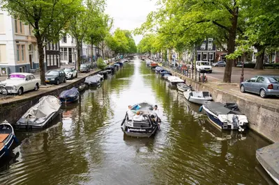 a group of boats in a canal with parked cars at PREMIER SUITES Amsterdam in Amsterdam