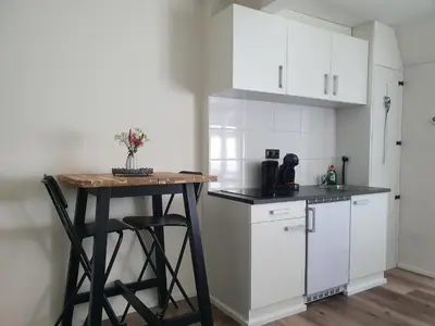 a kitchen with white cabinets and a small table at Studio Adanni in Zandvoort