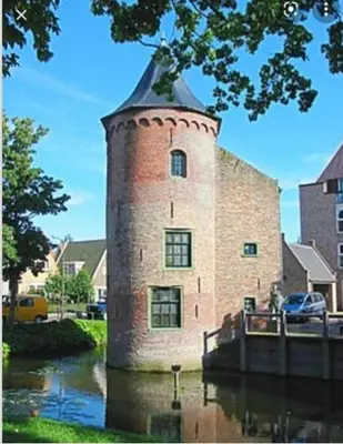 a brick building with a tower in the water at Huisje Finn, met grote tuin en veel privacy in Dirkshorn
