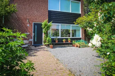a garden in front of a brick building with a door at Vakantiehuis Drie Dennen in Bergen