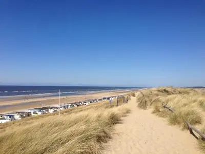 a sandy path to a beach with a bunch of cars at Westenwind in Egmond aan Zee