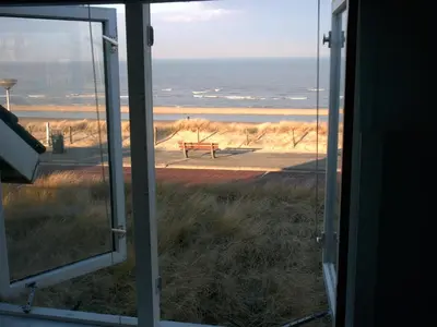 a view of a bench from a window with the ocean at Zeeduin - fantastisch uitzicht op zee in Bergen aan Zee