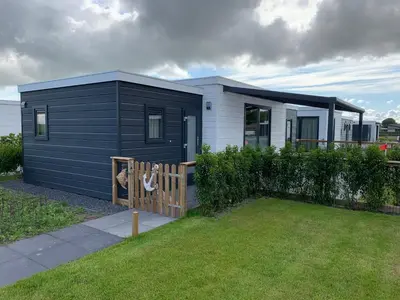a black and white tiny house with a fence at Vakantiepark Zijpersluis in Burgerbrug