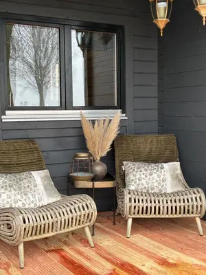 two wicker chairs and a table on a porch at Landelijk gelegen houten huisje in Opperdoes