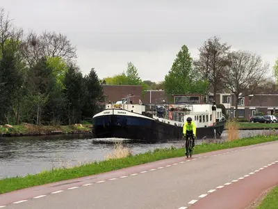 a person riding a bike down a road next to a boat at Hotelboat Sarah in Amsterdam