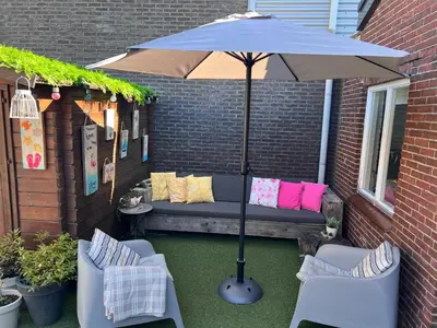 a patio with an umbrella and two chairs and a couch at Finca Noordwijk met privé tuin, dichtbij strand in Noordwijk