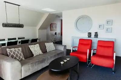 a living room with a couch and two red chairs at Appartement Spoorklokken in Bergen aan Zee