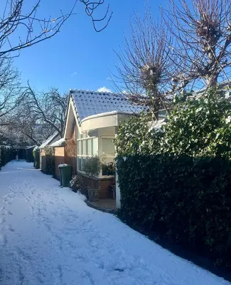 a house with snow on the ground next to a hedge at Prins Heerlijk in Sassenheim
