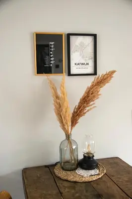 a table with a vase with dry grass and a candle at huisje de Strandjutter in Katwijk aan Zee