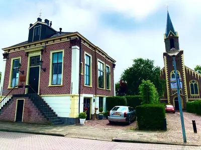 a building with a car parked in front of a church at B&B 't Raethuys in Dirkshorn
