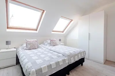a white bedroom with a bed and two windows at Sunny Spacious Apartment De Bijenkorf in Zandvoort