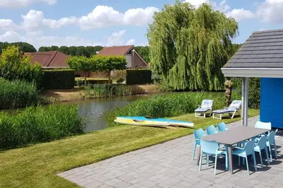 a patio with a table and chairs next to a river at The Blue House - Luxurious Waterfront Villa Zeewolde in Zeewolde