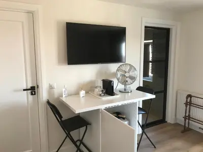 a white desk with a fan and a tv on a wall at Long Beach Rooms Zandvoort in Zandvoort