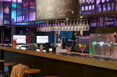 a bar with wine glasses hanging above it at Moxy Amsterdam Schiphol Airport in Hoofddorp