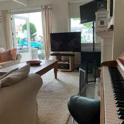 a living room with a couch and a piano at Holiday home at the water, fire place, boat and SUP rent, near Amsterdam in Aalsmeer