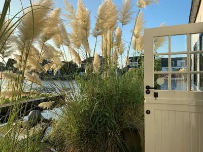 a white door in a garden with tall grass at Holiday home at the water, fire place, boat and SUP rent, near Amsterdam in Aalsmeer