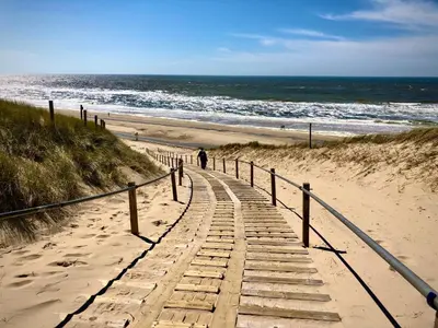a person walking down a wooden path to the beach at Strandhuis Everts in Egmond aan Zee