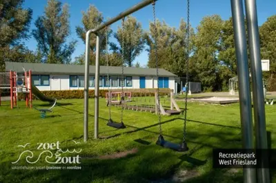 a playground with swings in the grass in front of a building at Wellness Bungalow Bolder 5p Amsterdam and the beach in Opmeer