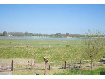 a fence in front of a field with a lake at Appartement RoMi in Koedijk