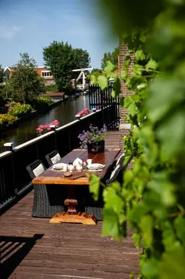 a wooden table and chairs on a deck next to a river at Oude Postkantoor de Rijp in De Rijp