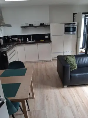 a living room with a black couch and a kitchen at Zomerhuis Carolina in Egmond aan Zee