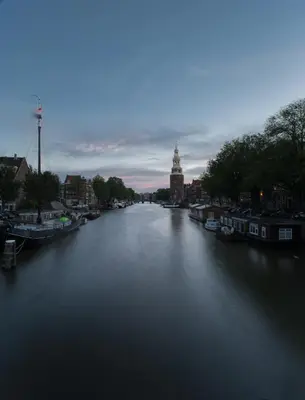 a river with boats and a clock tower in the distance at Anna Houseboat in Amsterdam