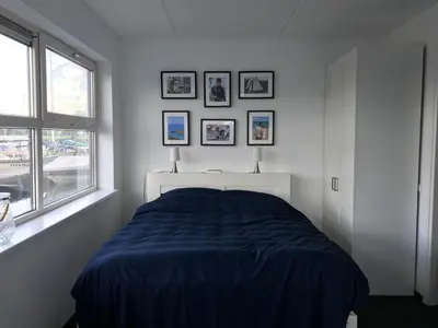 a white bedroom with a bed and a window at The Boathouse with boat in Aalsmeer