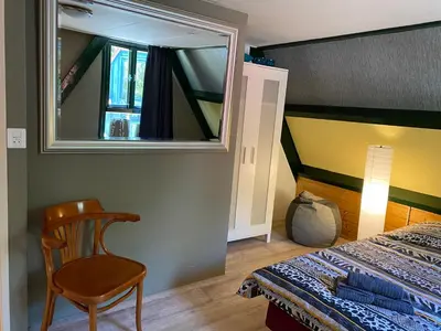 a bedroom with a bed and a mirror and a chair at Uniek vakantiehuisje in rustige en groene omgeving in Nieuwe-Niedorp