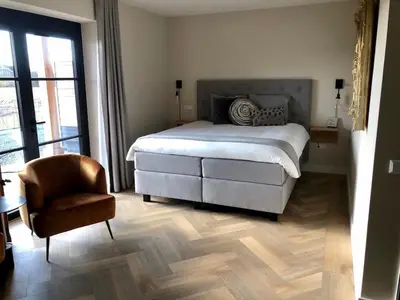 a bedroom with a large bed and a chair at B&B de Cley in Noordwijk