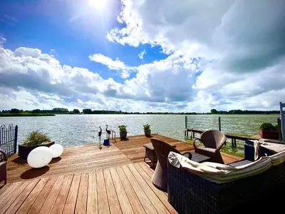 a dock with chairs and a boat on the water at Ferienhaus mit wundervollem Seeblick Ferienpark Vislust Ijsselmeer in Wervershoof
