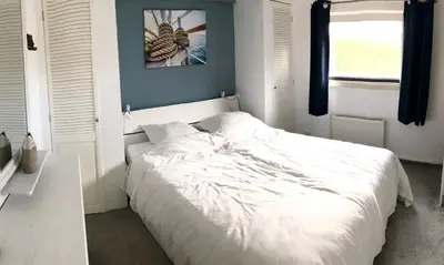 a bedroom with a white bed and a window at Ferienhaus mit wundervollem Seeblick Ferienpark Vislust Ijsselmeer in Wervershoof