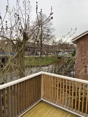 a wooden balcony with a tree and a building at Tinyhouse Woody at the Water in Zaandam