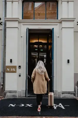 a woman walking out of a building with a suitcase at The Nox Hotel in Utrecht