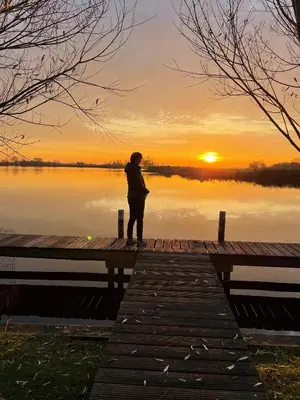 a person standing on a dock watching the sunset at Vakantie huis aan het water in Rijpwetering