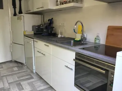 a kitchen with white cabinets and a sink and a refrigerator at De Linden in Egmond aan Zee