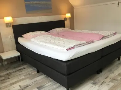 a large bed with a black frame and pink sheets at De Linden in Egmond aan Zee