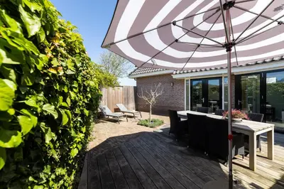 a patio with a table and an umbrella at Kustlijn vakantiewoning in Egmond aan den Hoef