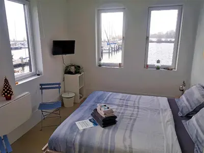 a bedroom with a bed and windows with a view of the water at Kaap Hoorn Club Bed en Breakfast in Hoorn