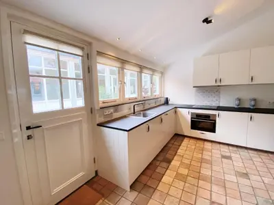 a kitchen with white cabinets and a sink and windows at Cozy historical Cottage (Huisje HèHè) in Wassenaar