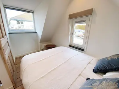 a small bedroom with a bed and two windows at Cozy historical Cottage (Huisje HèHè) in Wassenaar