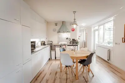 a kitchen with white cabinets and a wooden table and chairs at De Lijsterhof in Zandvoort