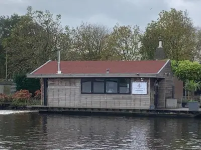 a house on a dock next to a body of water at Aangenaam op de Rijn, woonboot, inclusief privé sauna in Alphen aan den Rijn
