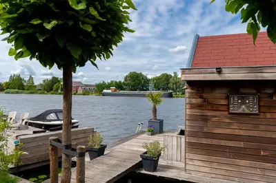 a house on a dock with a boat on the water at Aangenaam op de Rijn, woonboot, inclusief privé sauna in Alphen aan den Rijn